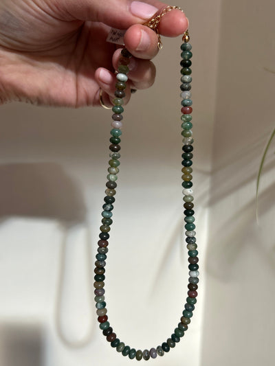 Hand holding a beaded necklace with a neutral background