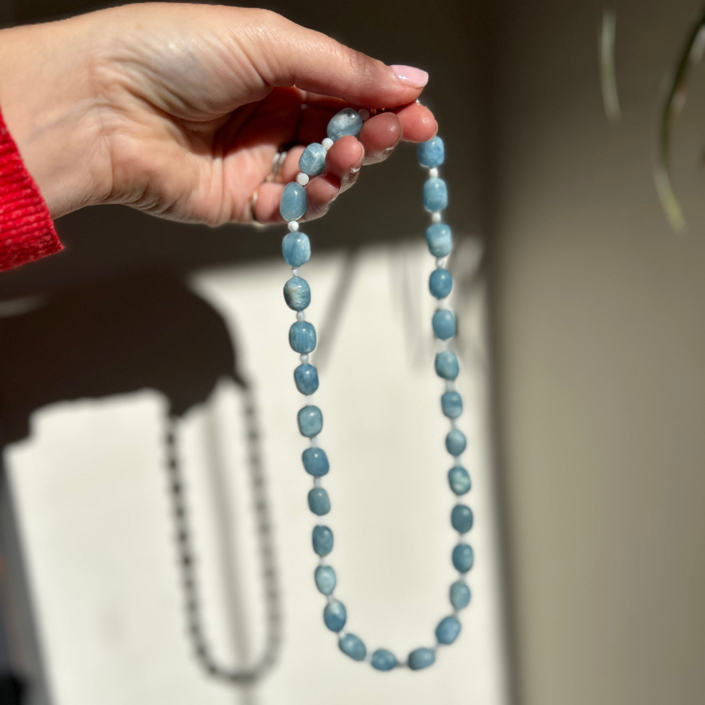 Hand holding a string of blue beads against a neutral background