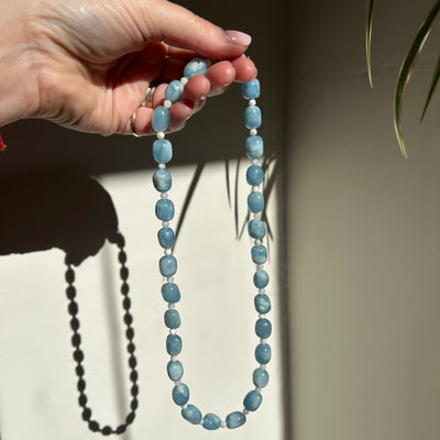 Hand holding a blue beaded necklace with a neutral background