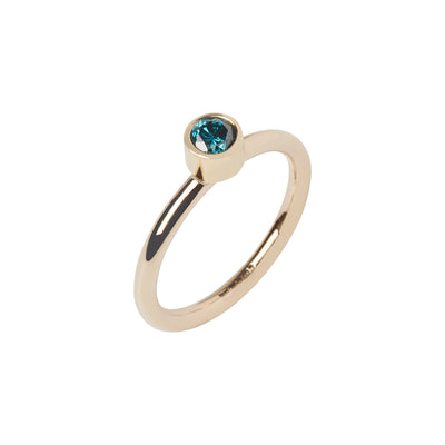 A blue round faceted diamond set in a gold bezel setting on a gold ring band with a white background