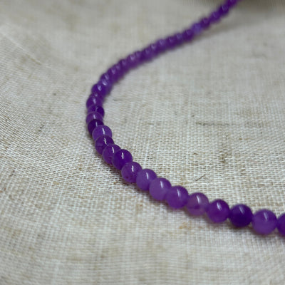 Dyed purple jade round bead necklace on linen background