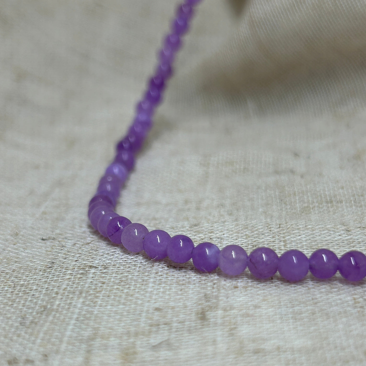 Dyed purple jade bead necklace on linen background