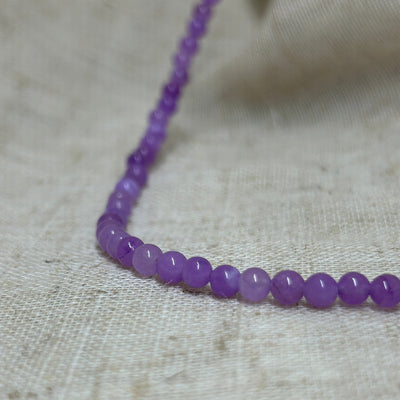 Dyed purple jade bead necklace on linen background