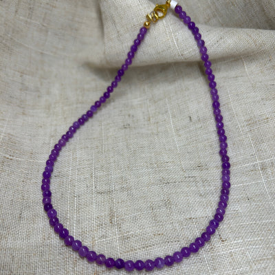 Dyed purple jade bead necklace on linen background