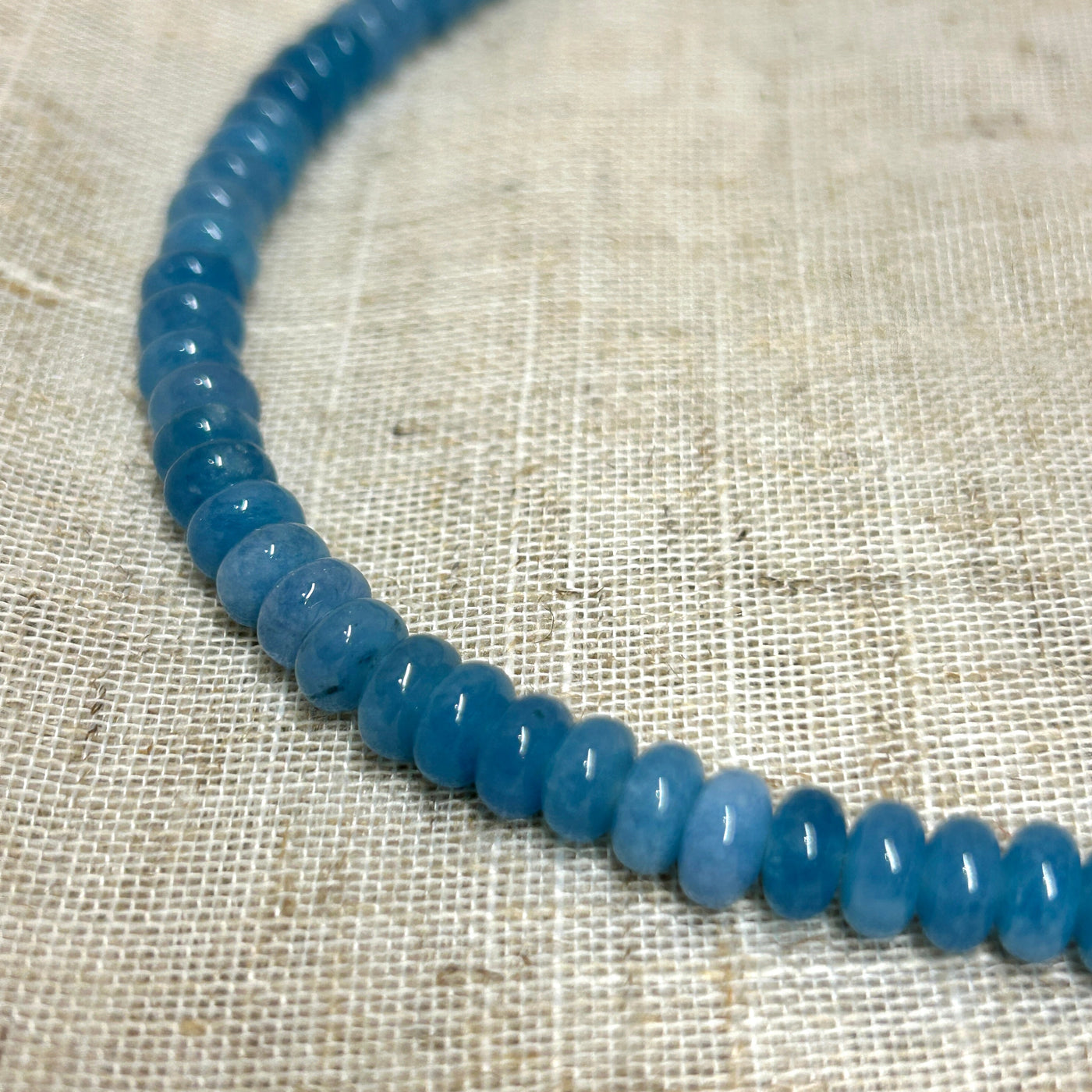 Necklace with blue beads on a textured beige fabric background
