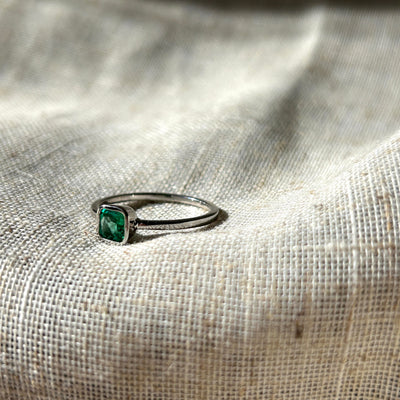 Platinum ring with a green emerald gemstone on a textured fabric background