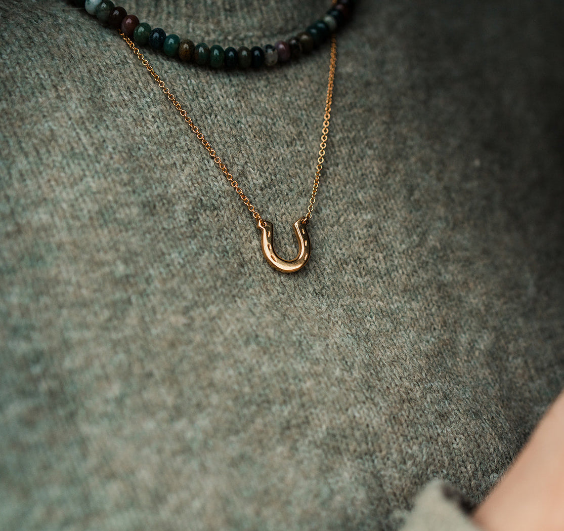 Gold plated horseshoe pendant worn by a woman with a green jumper