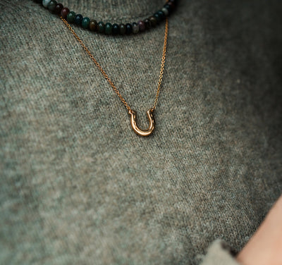 Gold plated horseshoe pendant worn by a woman with a green jumper
