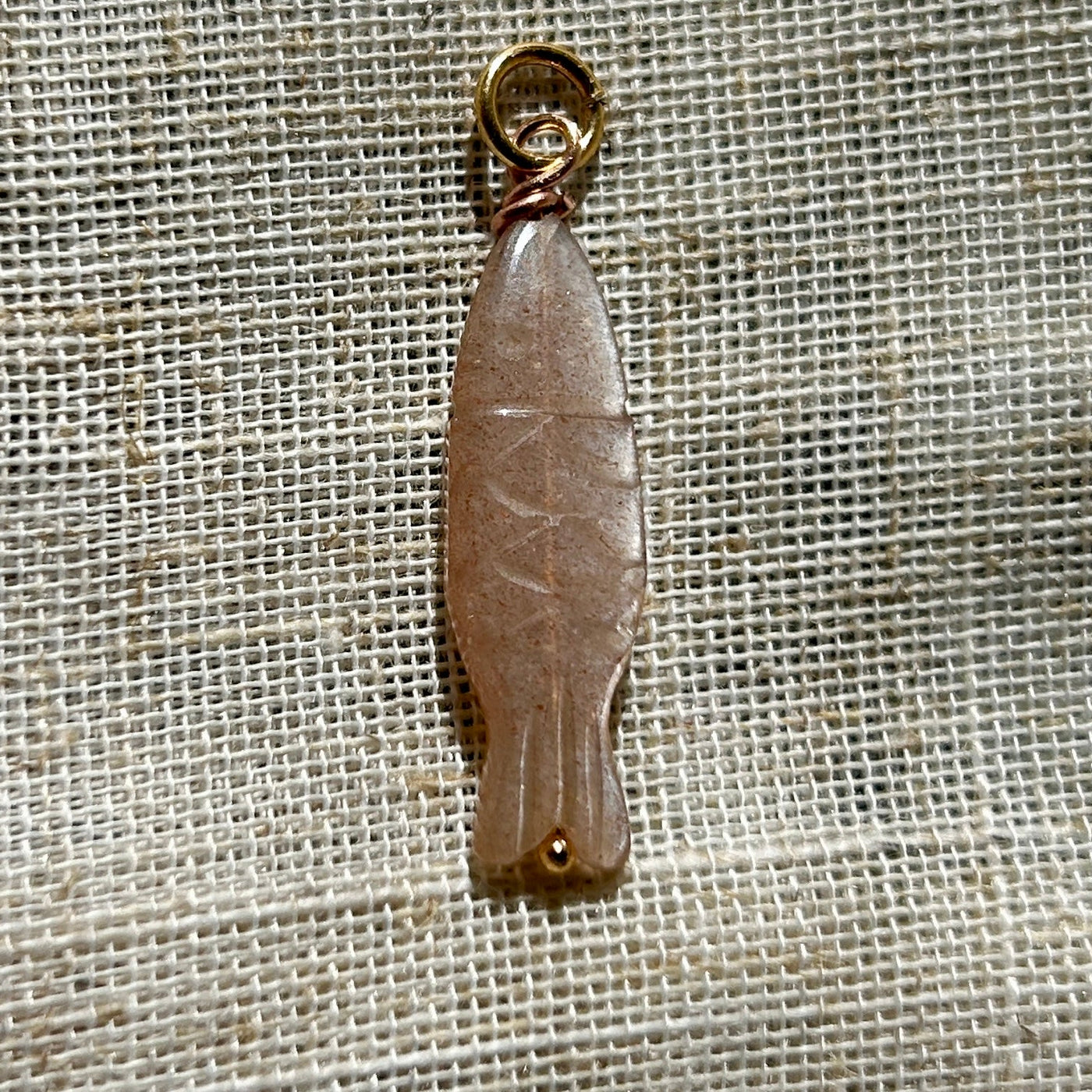 Peach moonstone pendant with gold ring on a textured beige background