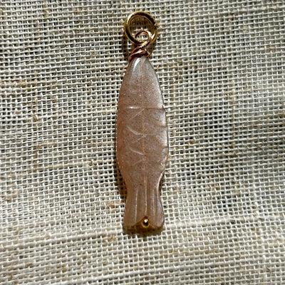 Peach moonstone pendant with gold ring on a textured beige background