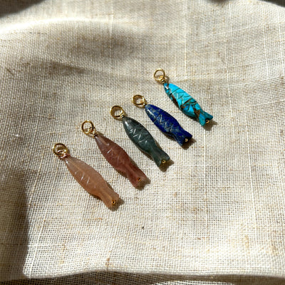 Set of colourful gemstone fish pendants on a textured fabric background