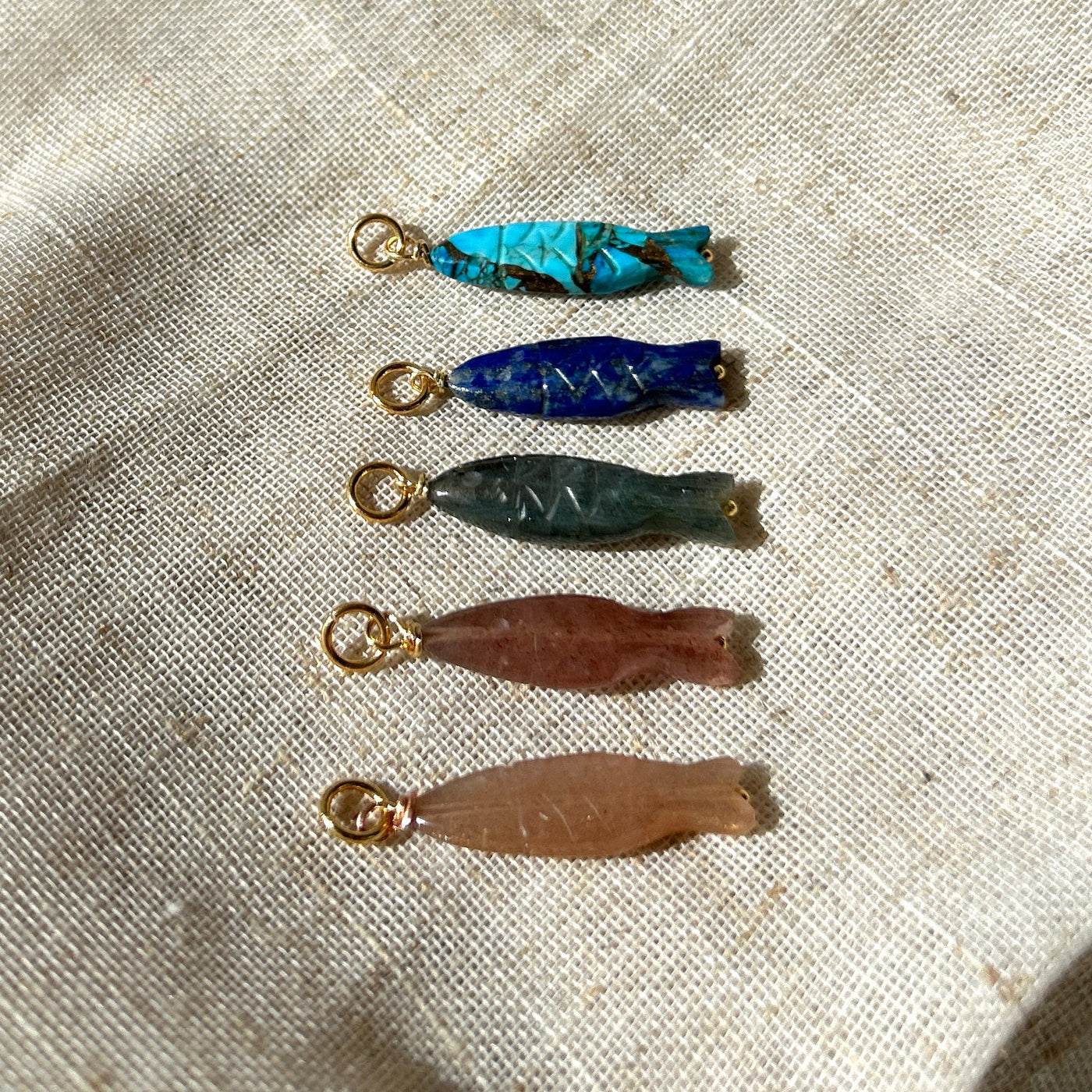 Set of five colourful gemstone fish charms on a textured fabric background