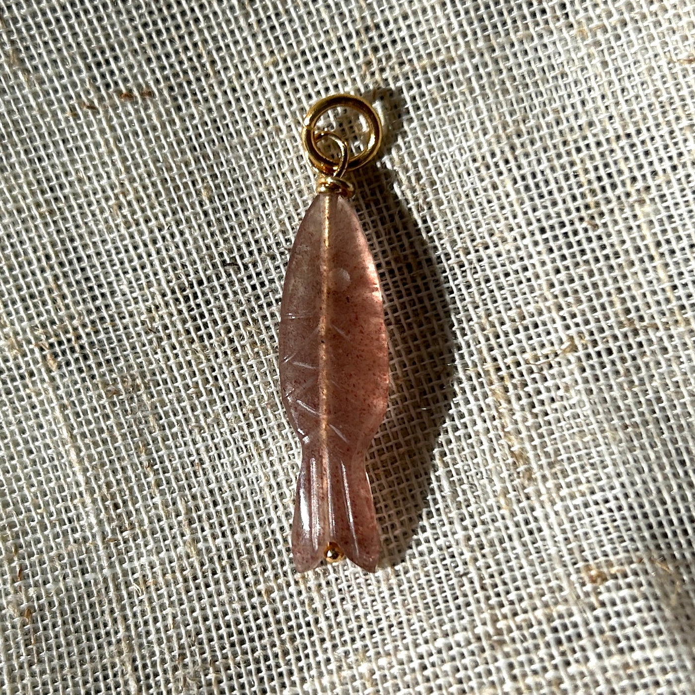 Strawberry quartz fish pendant on a textured beige fabric background