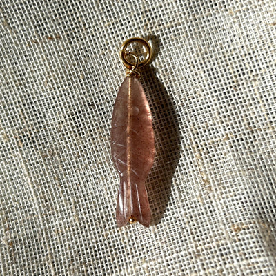 Strawberry quartz fish pendant on a textured beige fabric background