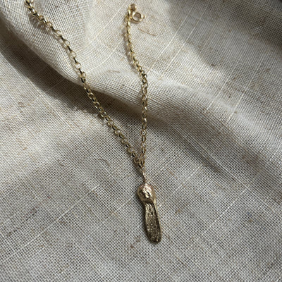 A 9ct yellow gold Sycamore Gap seed charm on a gold oval belcher chain bracelet on a textured linen background.