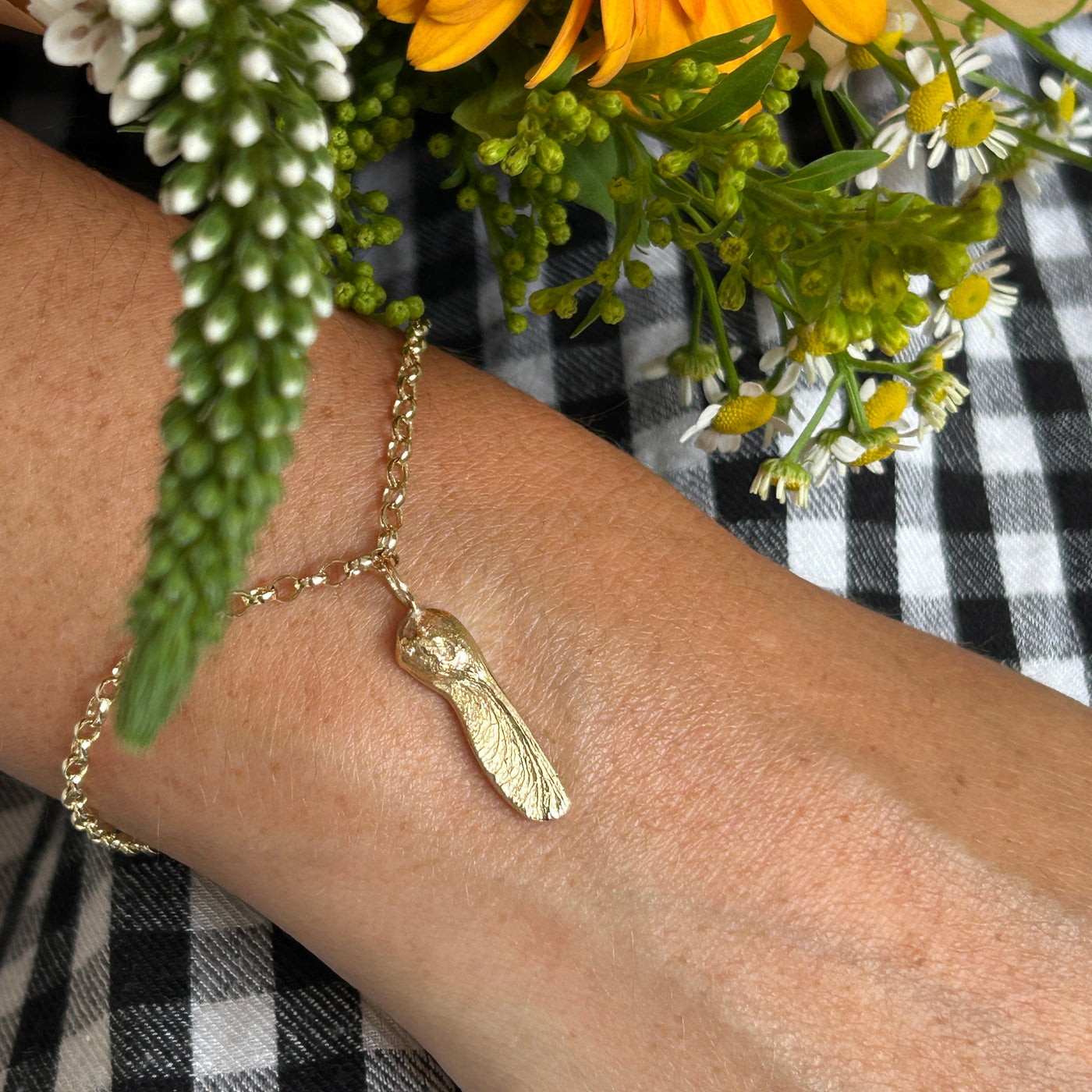 Gold bracelet on a wrist with a bouquet of flowers and checkered fabric in the background