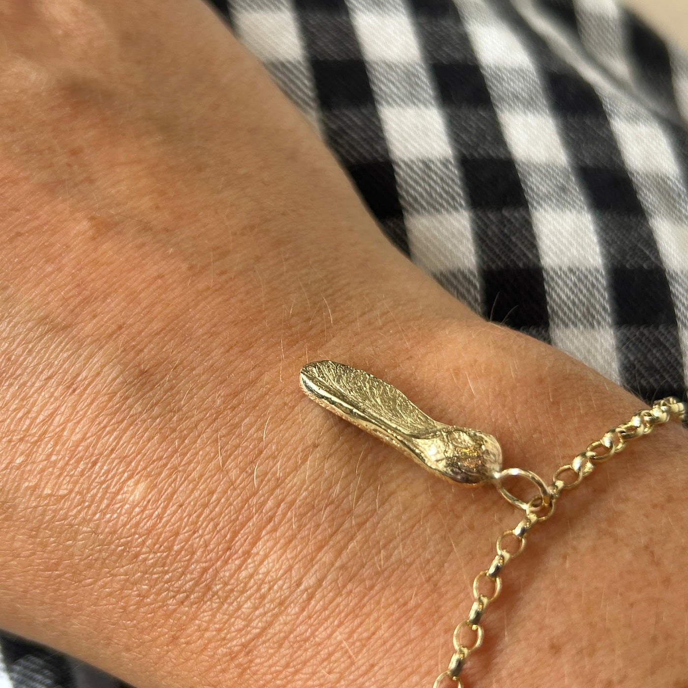 9ct yellow gold bracelet with a Sycamore Gap seed charm on a gold chain on a checkered background