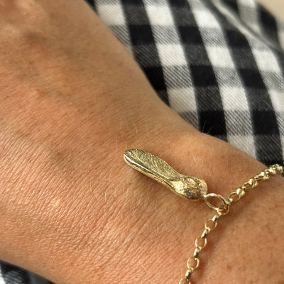 9ct yellow gold bracelet with a Sycamore Gap seed charm on a gold chain on a checkered background