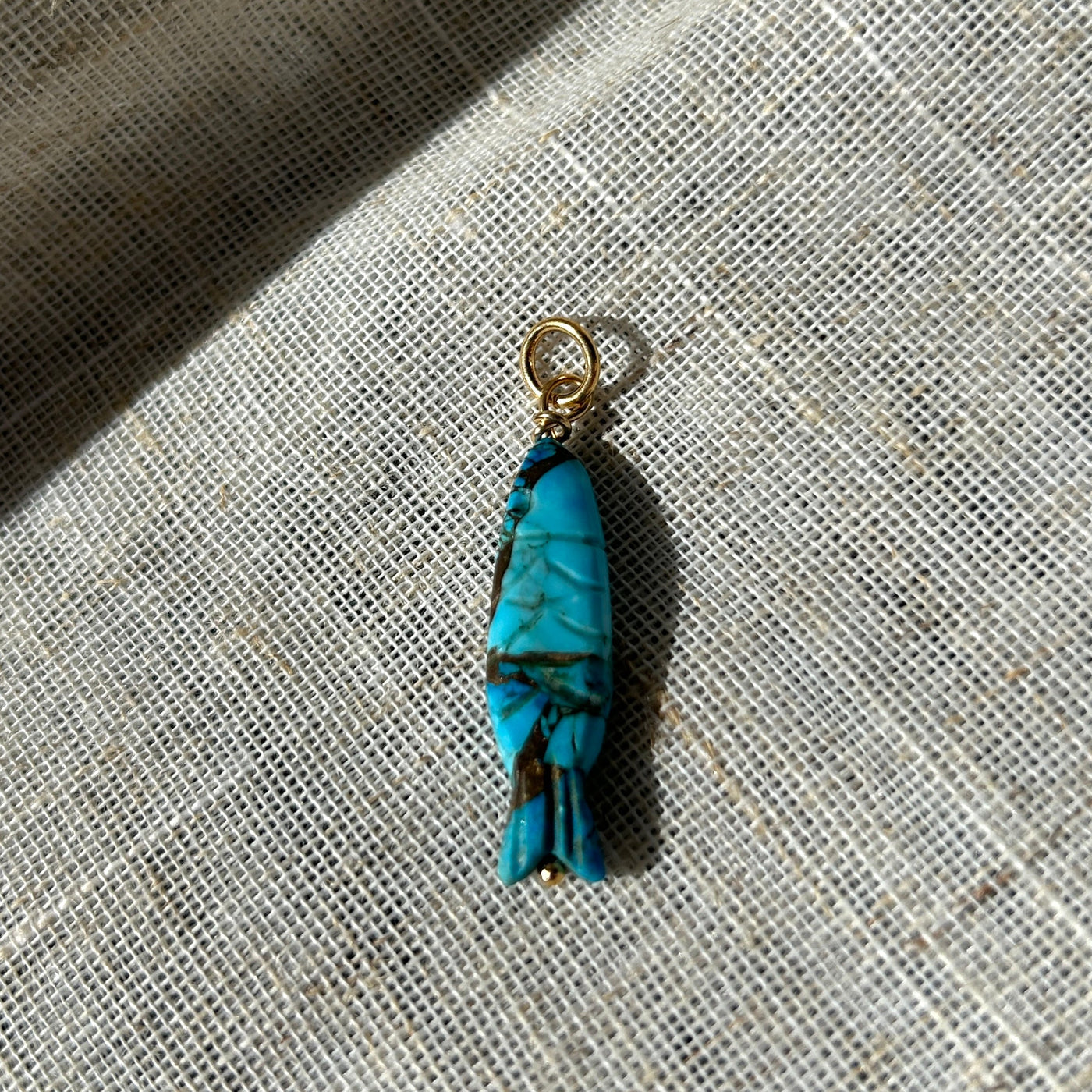 Turquoise pendant on a gold chain on a textured fabric background