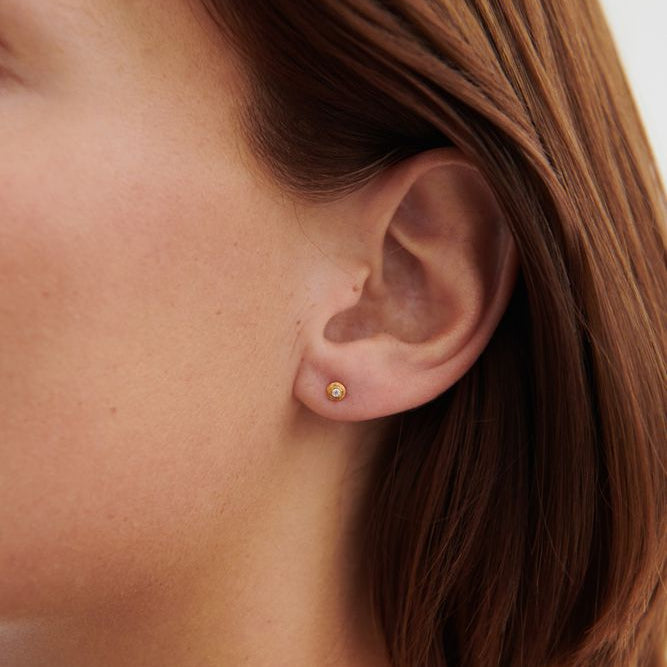 Close-up of a person wearing a gold earring with a blurred background