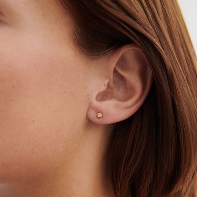 Close-up of a person wearing a gold earring with a blurred background