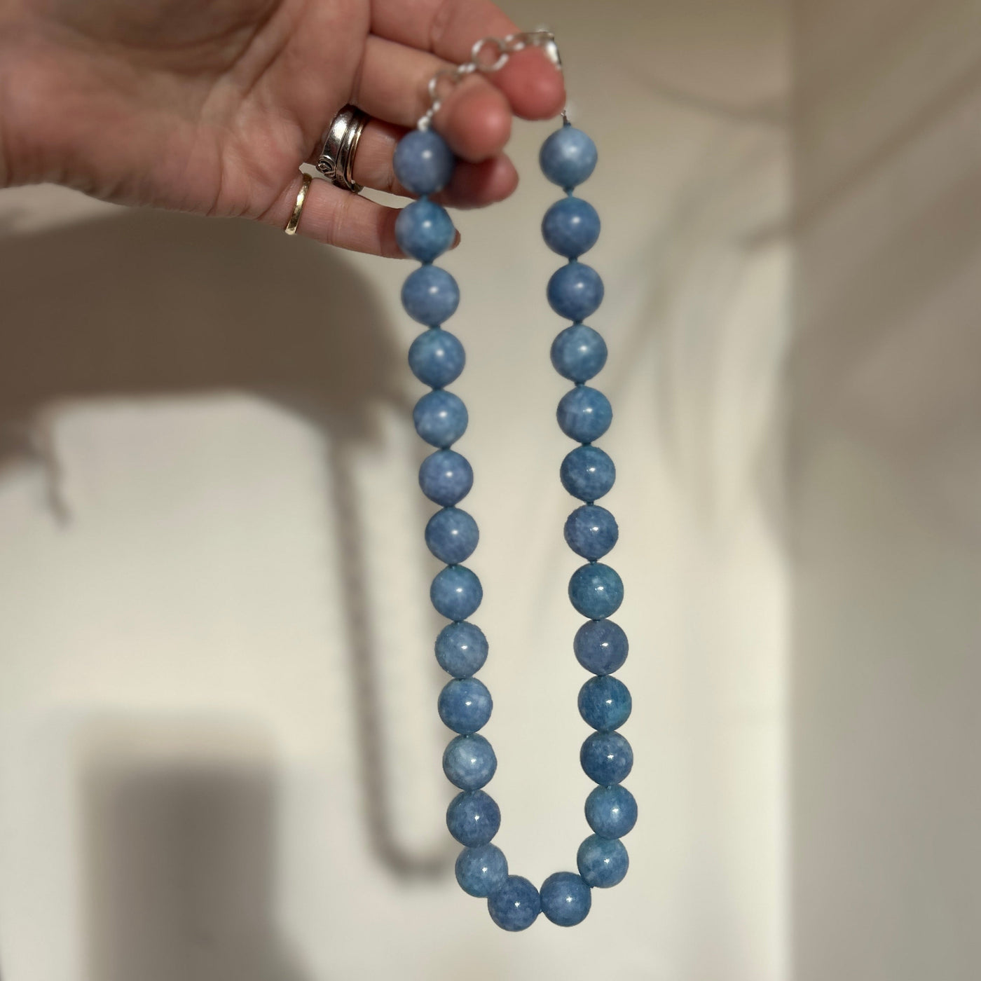Hand holding a blue beaded necklace against a neutral background