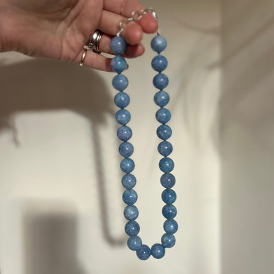Hand holding a blue beaded necklace against a neutral background