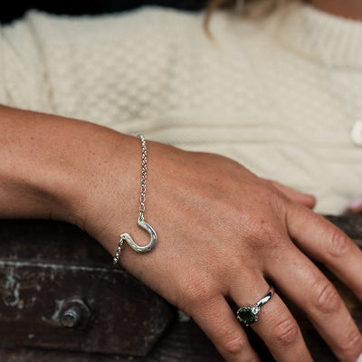 Close-up of a hand wearing a silver bracelet and ring on a wooden surface