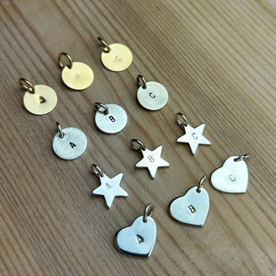 Collection of disk, star and heart shaped metal charms with stamped initials on a wooden surface