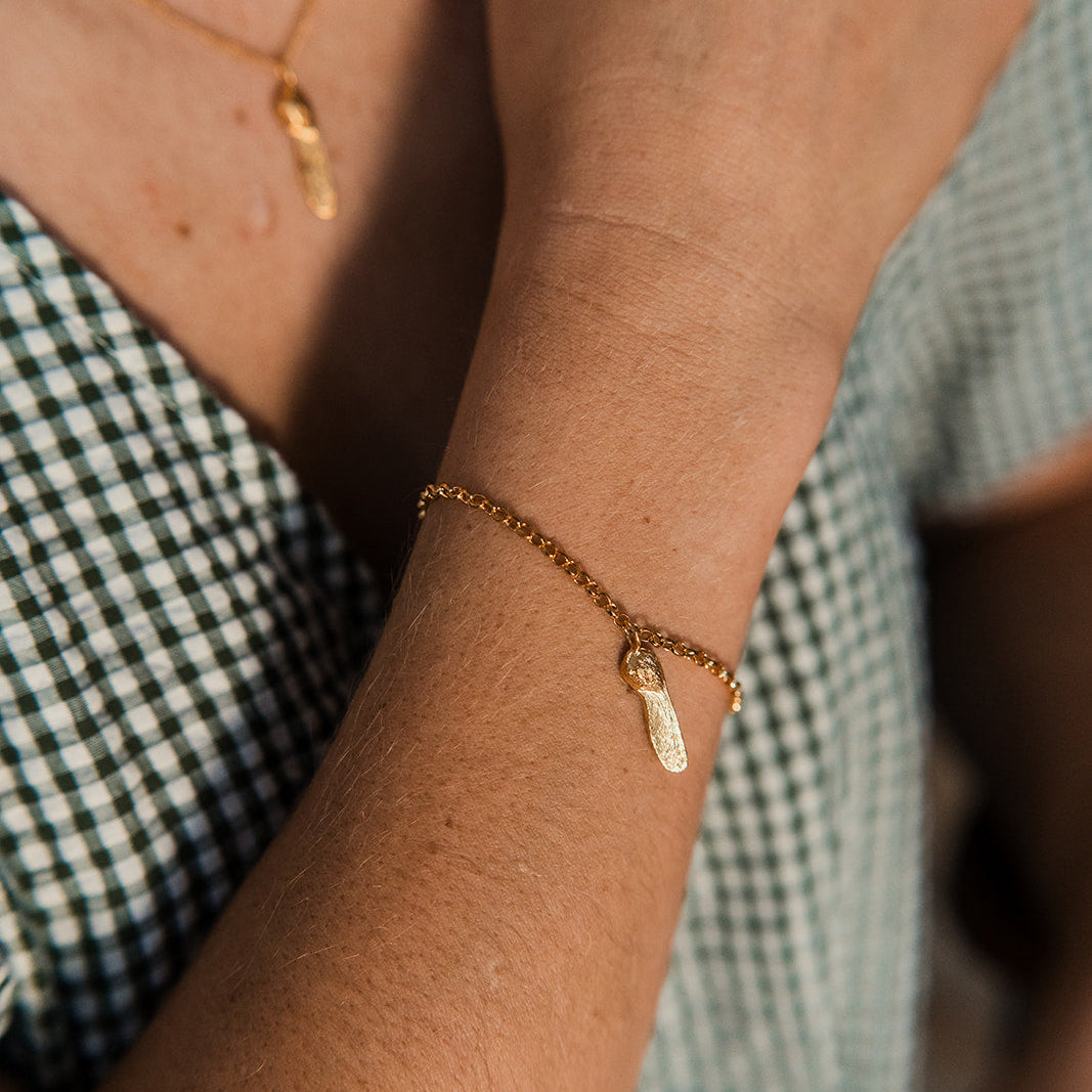 Close-up of a person's wrist wearing a gold bracelet with Sycamore Gap charm, against a blurred background.