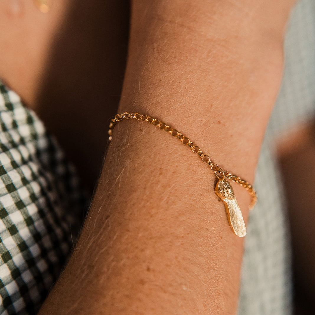 Gold bracelet with a small sycamore gap charm on a wrist, blurred background