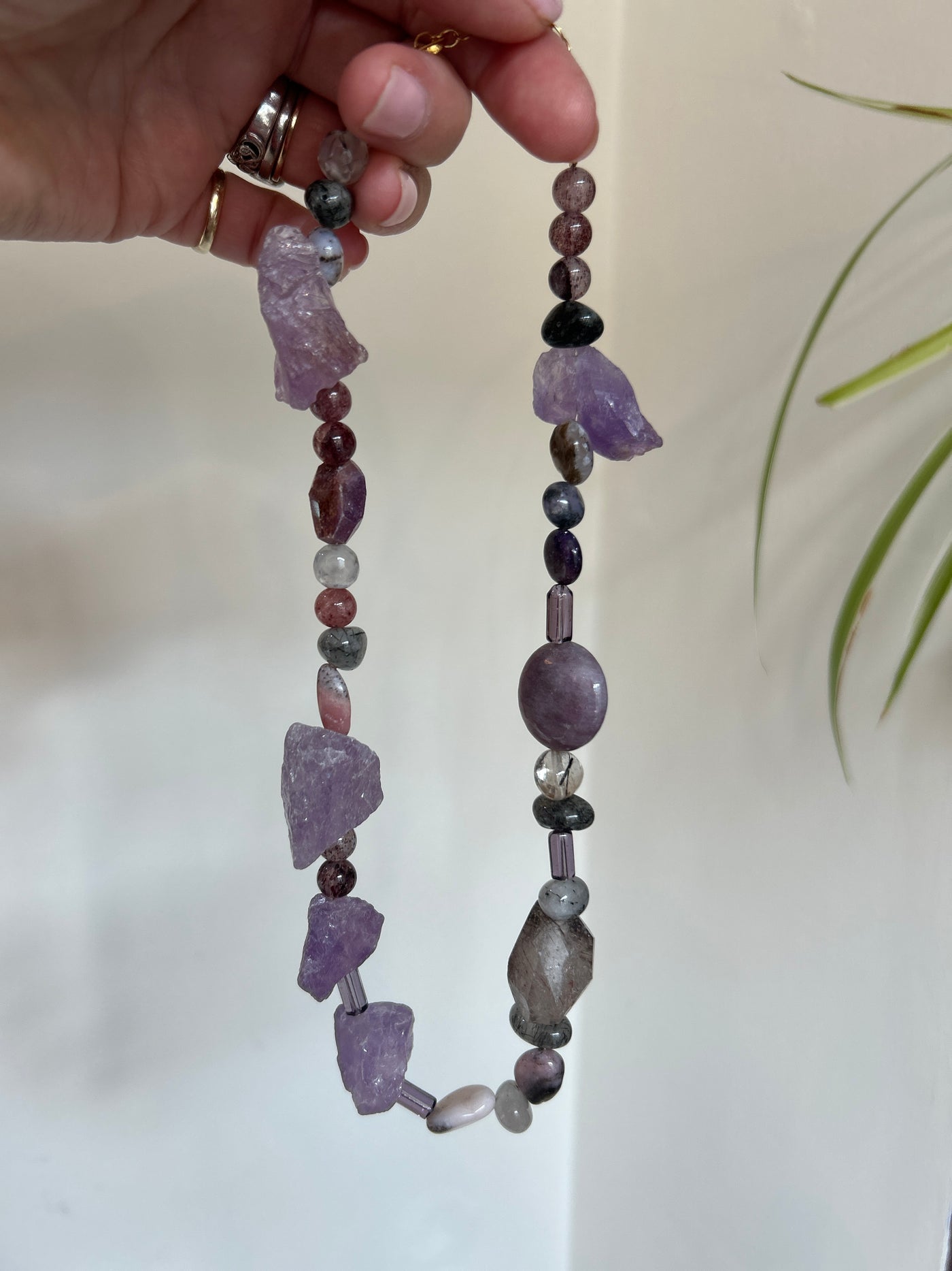 Hand holding a beaded necklace with purple and gray stones against a white background