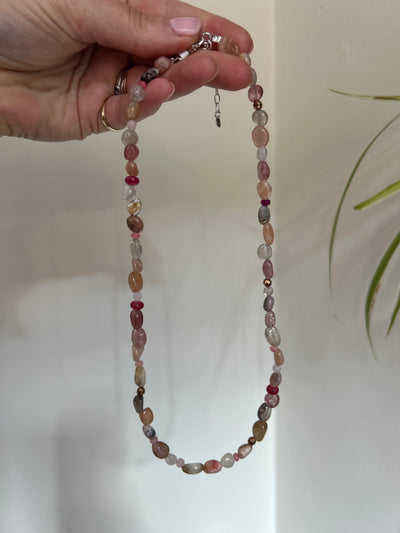 Beaded necklace held by a hand against a neutral background
