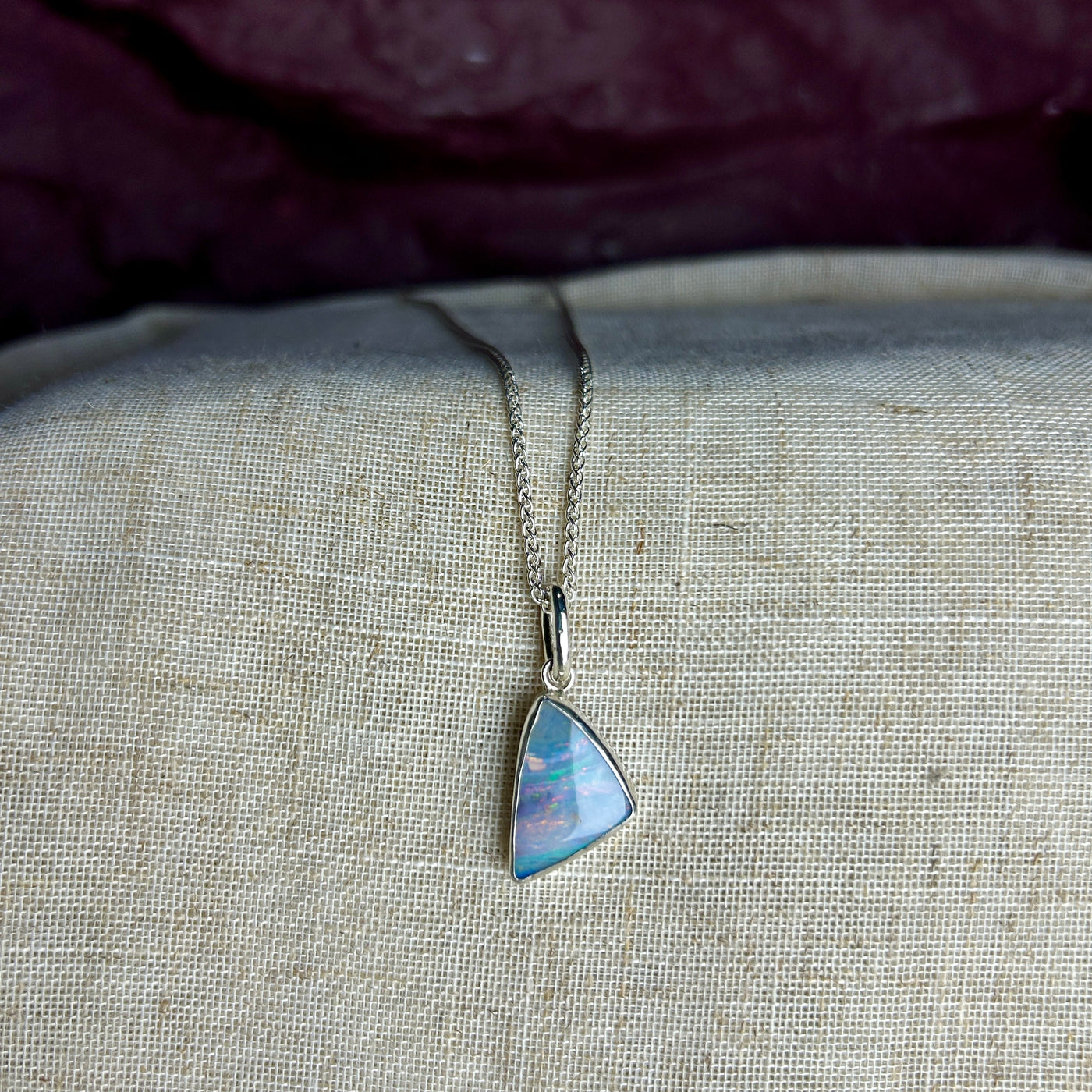 A triangular shaped blue Winton opal set into sterlilng silver with a large bail and spiga chain on a linen background 