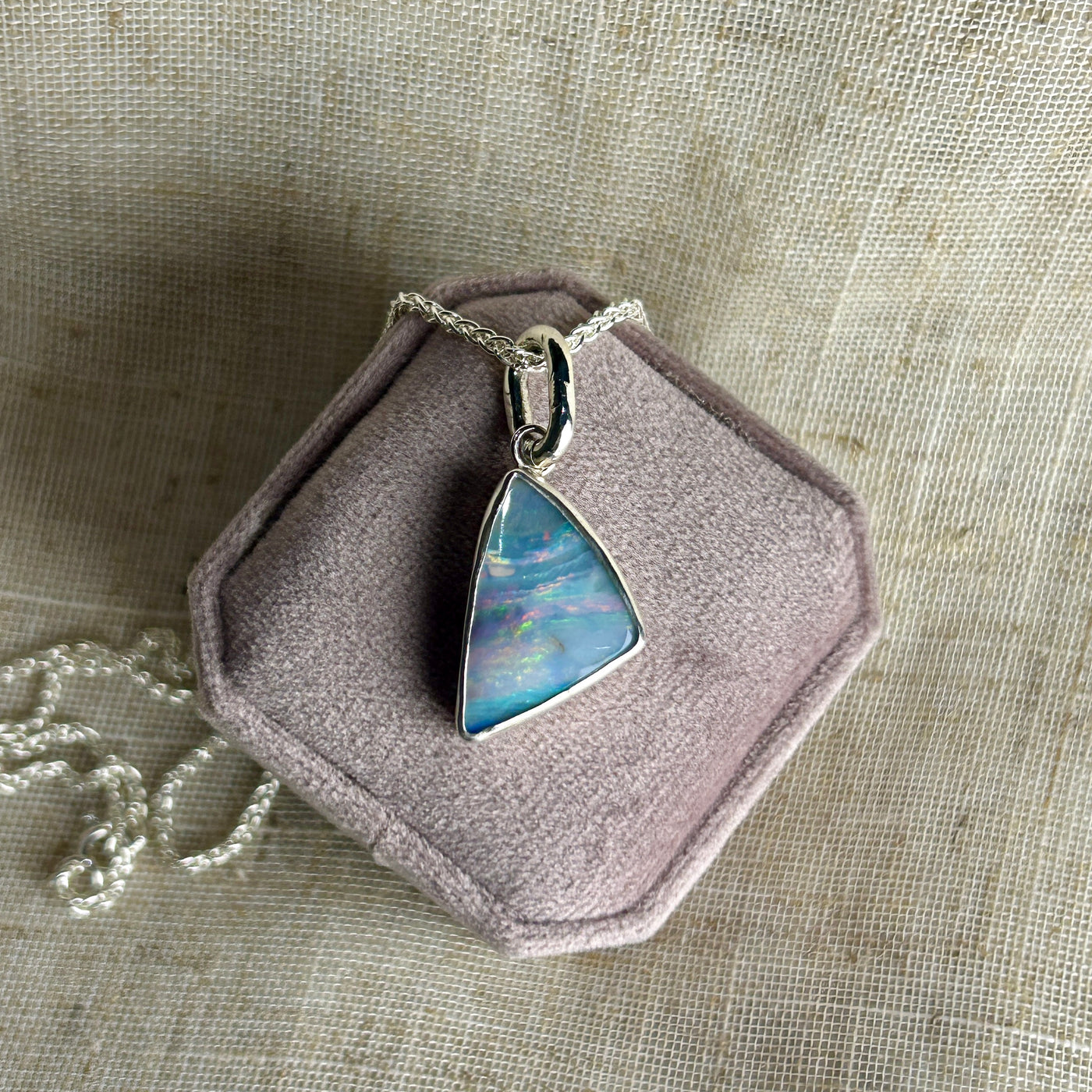 Blue opal in sterling silver on a silver chain  on a pink box on a linen background. 