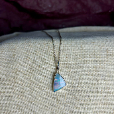 A triangular shaped blue Winton opal set into sterlilng silver with a large bail and spiga chain on a linen background 