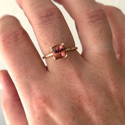 Gold ring with a pink gemstone on a person's finger against a neutral background