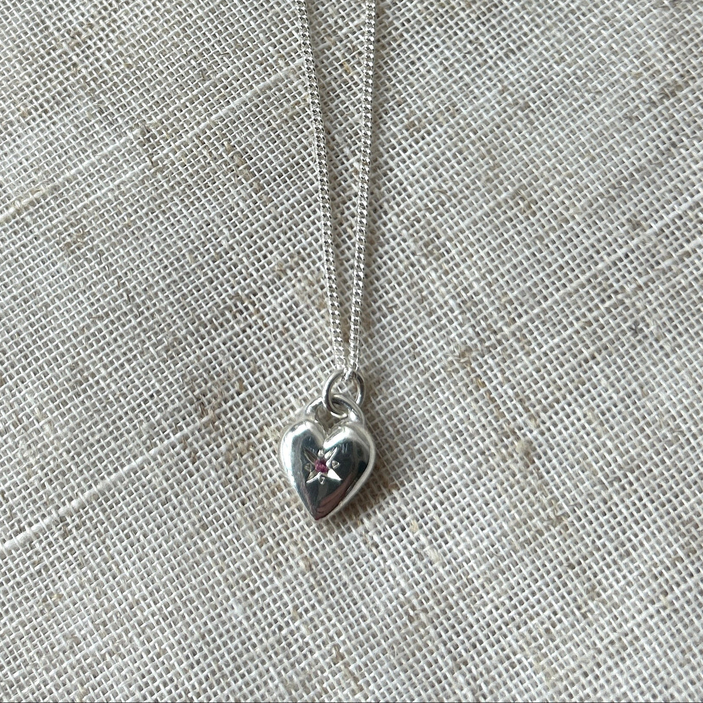 Silver heart-shaped pendant necklace on a gray fabric background star set with a pink tourmaline gemstone