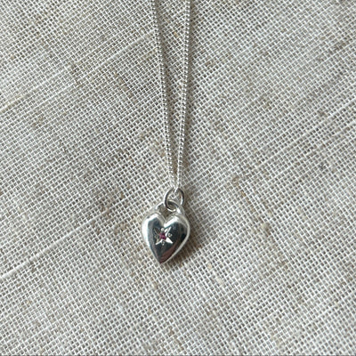 Silver heart-shaped pendant necklace on a gray fabric background star set with a pink tourmaline gemstone