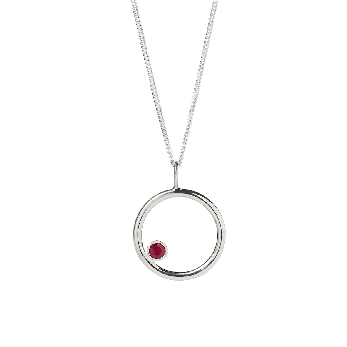 Silver circle pendant with offset bezel set 4mm red Ruby gemstone on a sterling silver curb chain on a white background. Handmade in Kirsty Taylor Goldsmiths in Northumberland