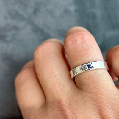Silver ring with a blue gemstone on a finger against a gray background