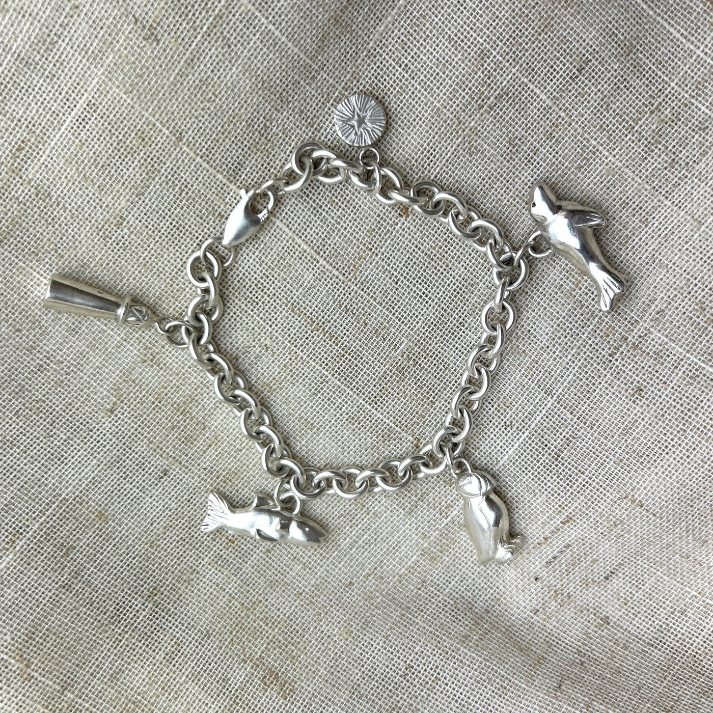 Silver Northumberland coastal charm bracelet on a textured fabric background