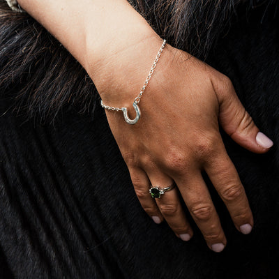 Hand wearing a  silver horseshoe bracelet and ring resting on a horse