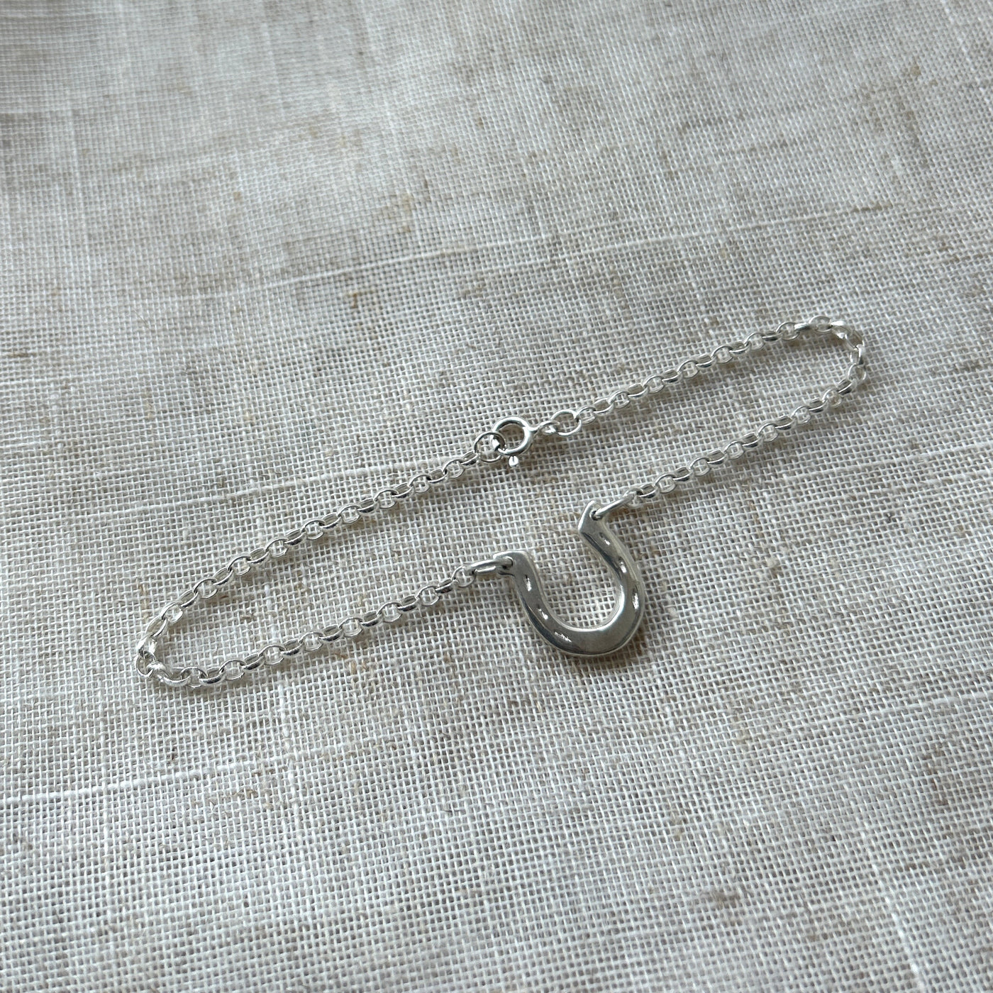 Silver horseshoe bracelet with a hook clasp on a textured grey fabric background