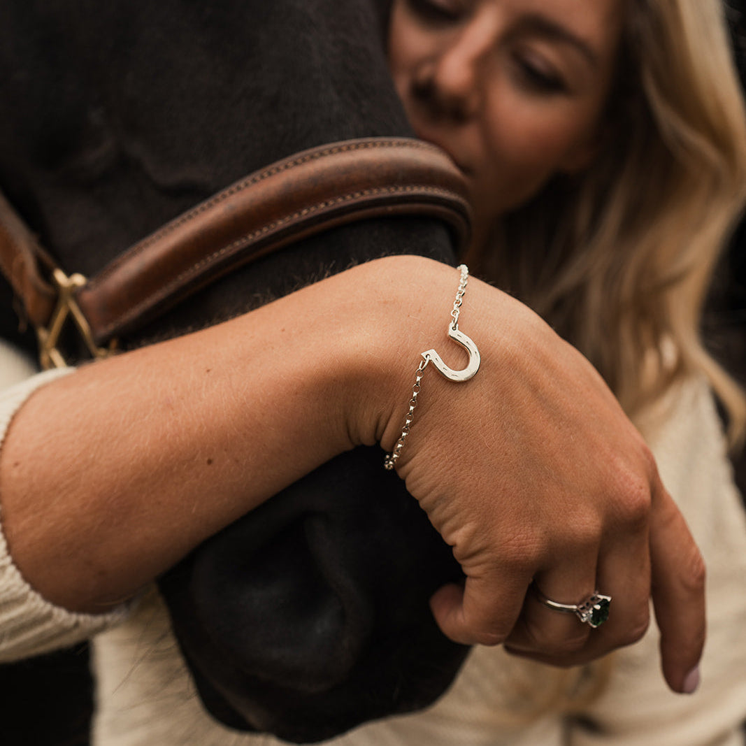 Person wearing a bracelet and ring, embracing a horse.