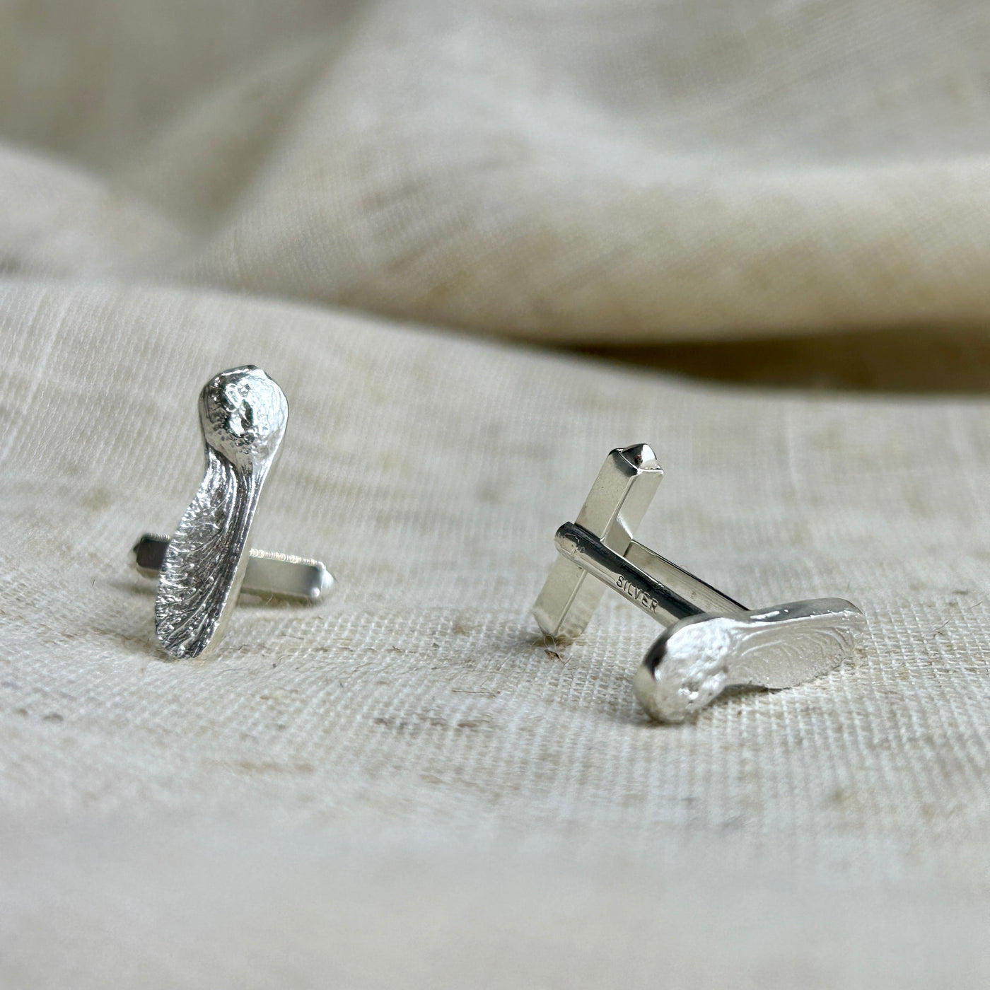 Silver Sycamore Gap cufflinks on a textured beige fabric background