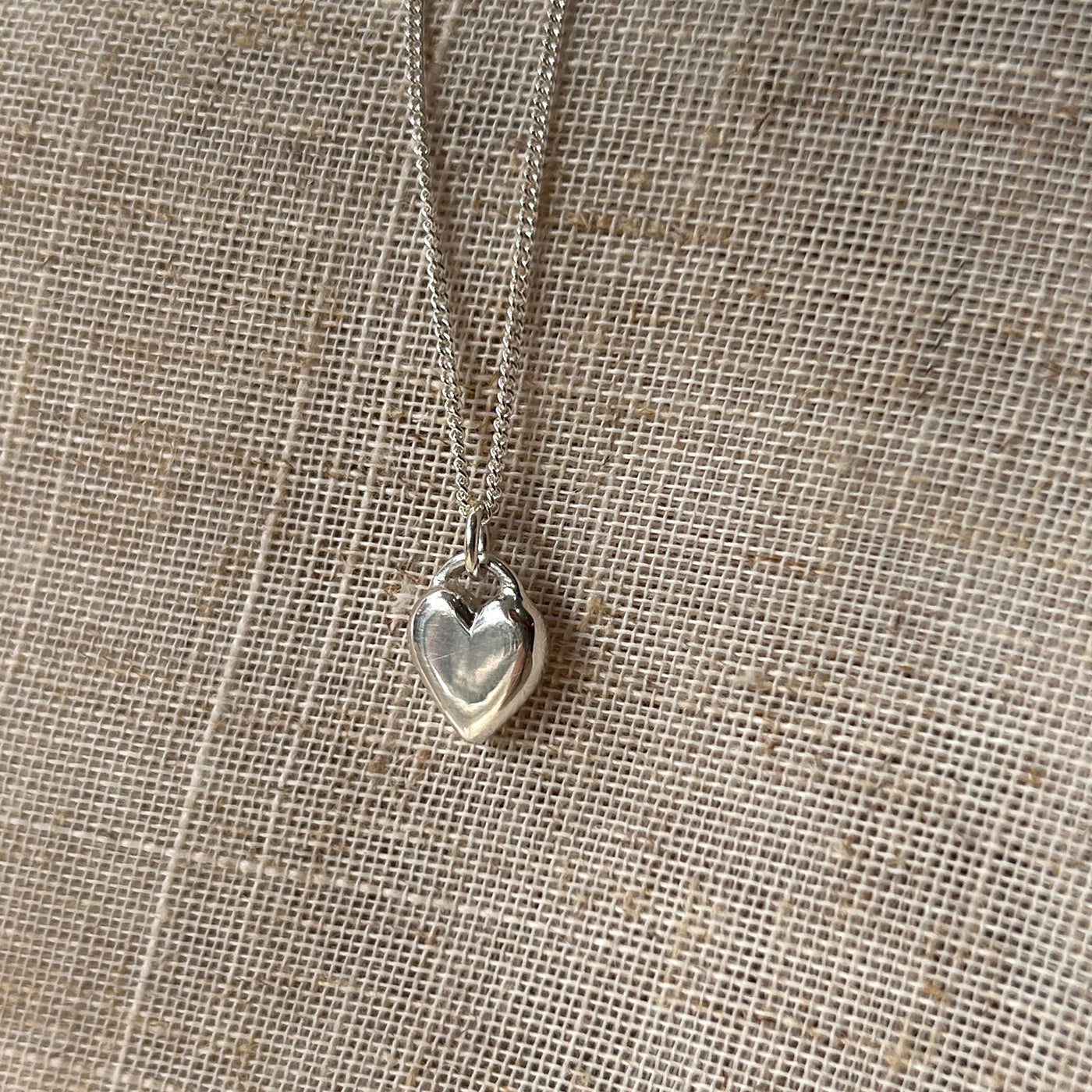 Silver heart-shaped pendant necklace on a textured beige fabric background