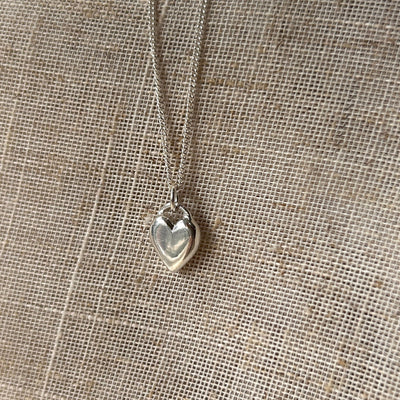 Silver heart-shaped pendant necklace on a textured beige fabric background