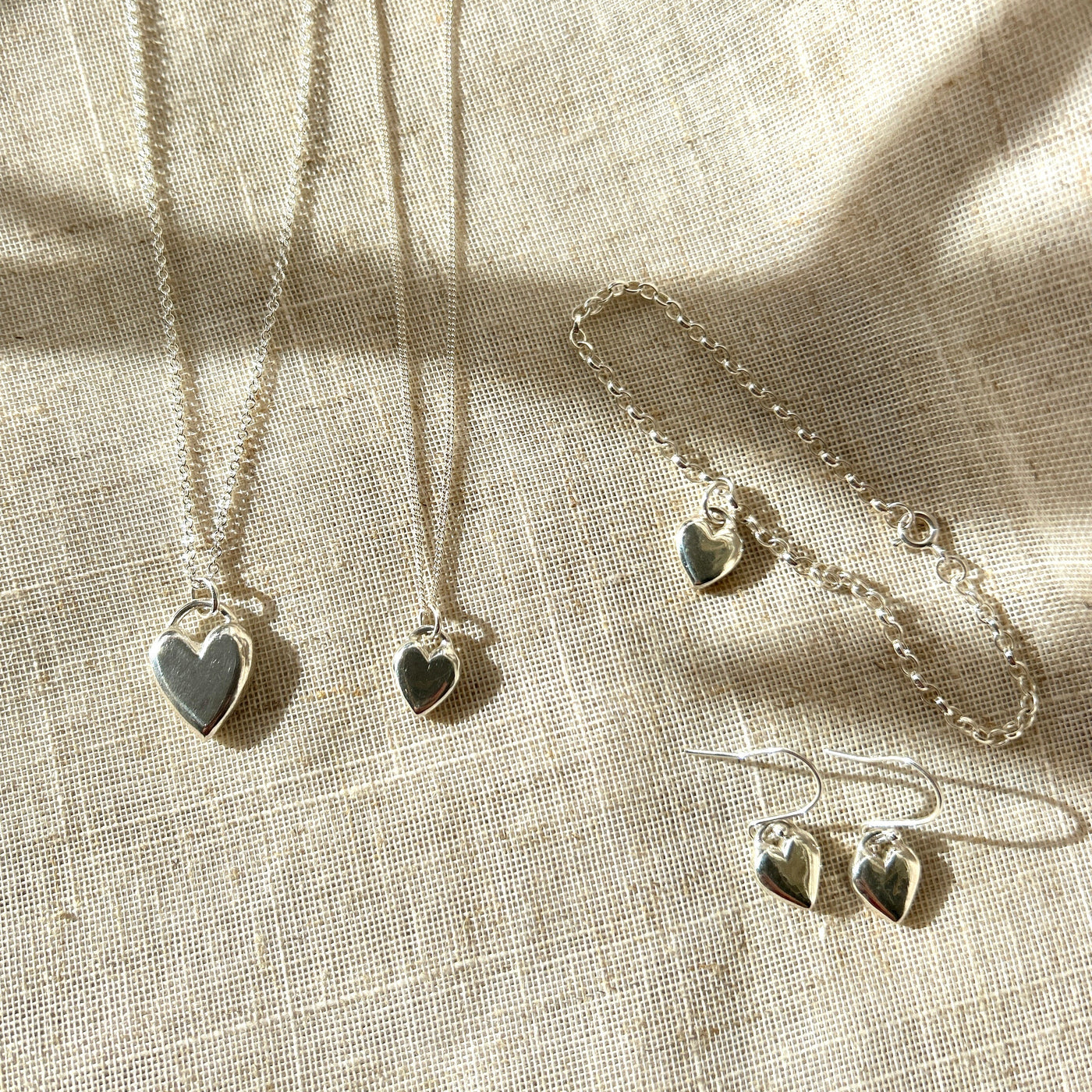 Silver jewellery set with heart-shaped pendants on a textured fabric background