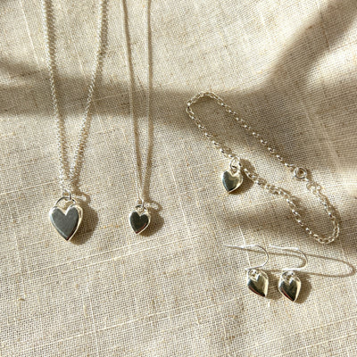 Silver jewellery set with heart-shaped pendants on a textured fabric background